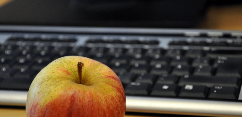 Ett äpple som ligger framför ett tangentbord.