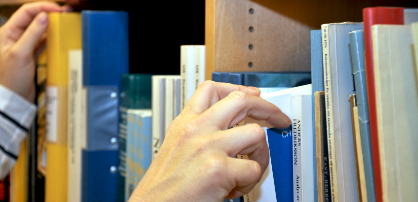 Händer som letar fram böcker i bokhylla. 