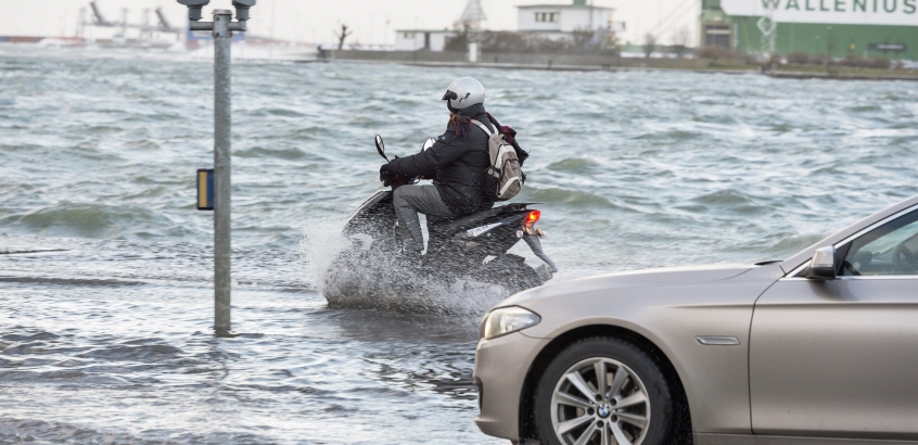 En bil och en moped som kör på en översvämmad väg.