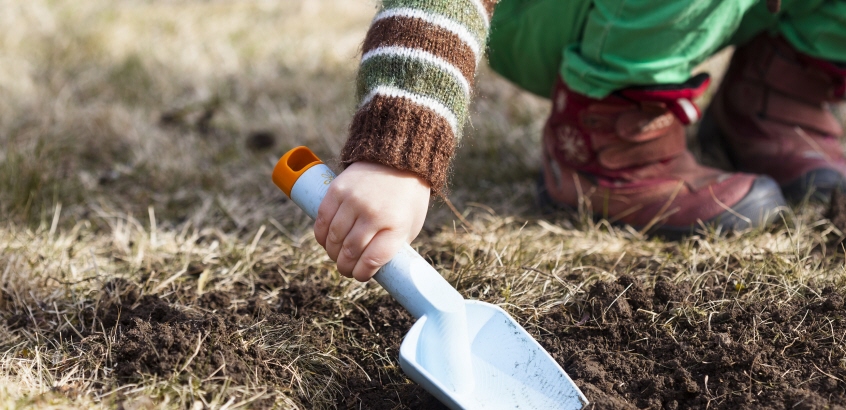 En barnhand som håller i en liten spade och gräver i jorden. 