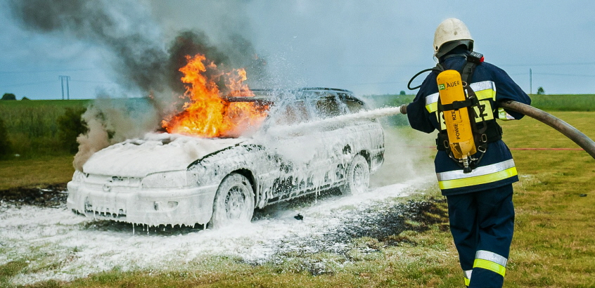 Två brandmän som sprutar skum på en brinnande bil.