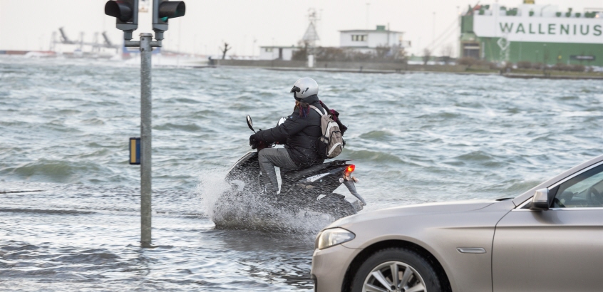 En bil och en moped som kör på en översvämmad väg.