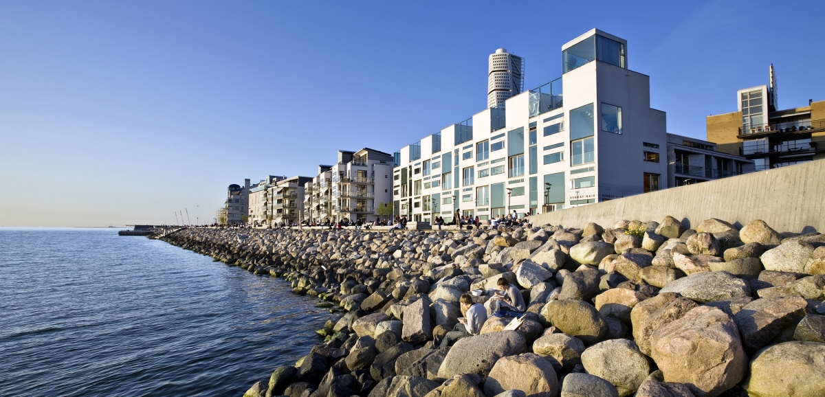 Lägenhetskomplex byggt intill vatten. Stenblock vid strandkanten skyddar mot vågor.