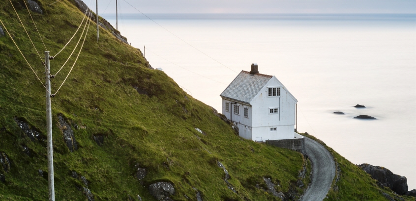 Ett ensamt hus byggt i en bergsslänt ner mot vatten.