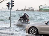 En bil och en moped som kör på en översvämmad väg.