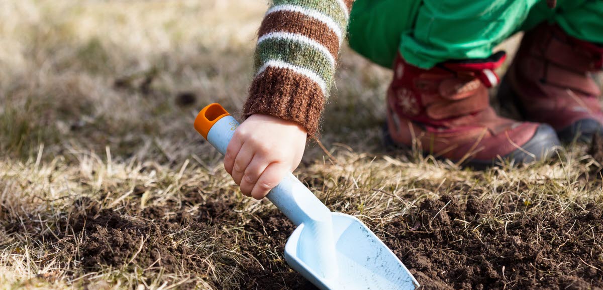 En barnhand som håller i en liten spade och gräver i jorden. 