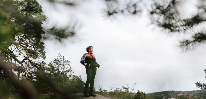 Kvinna står på klippa i skog och tittar bort